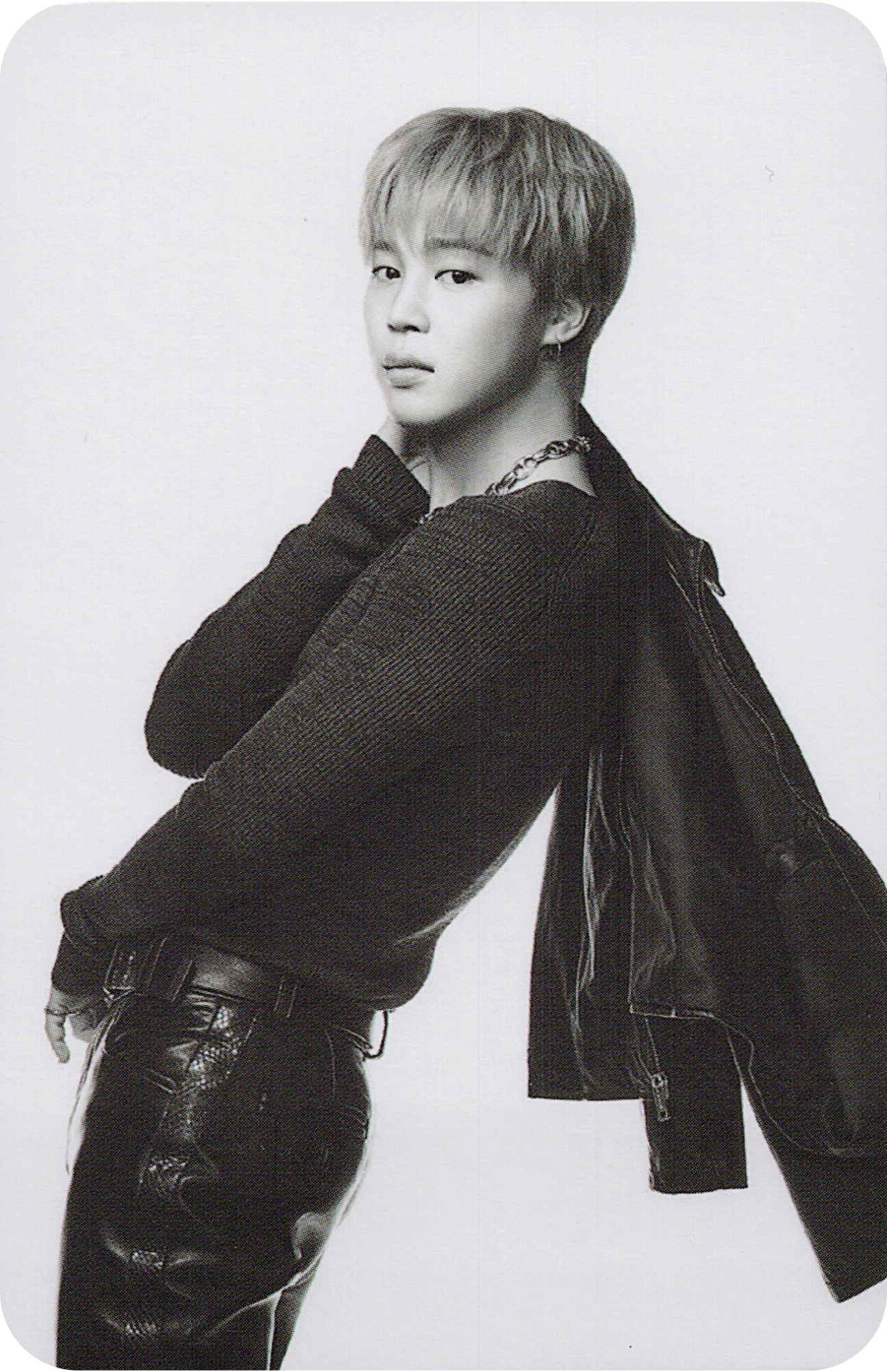 Black and white photo of BTS member Jimin wearing a jacket and pants on a plain background