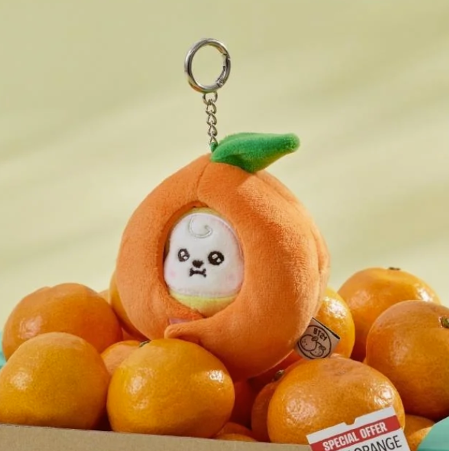 BTS BT21 Chimmy Plush keychain shaped like an orange with a cute face design, surrounded by real oranges on a light yellow background.