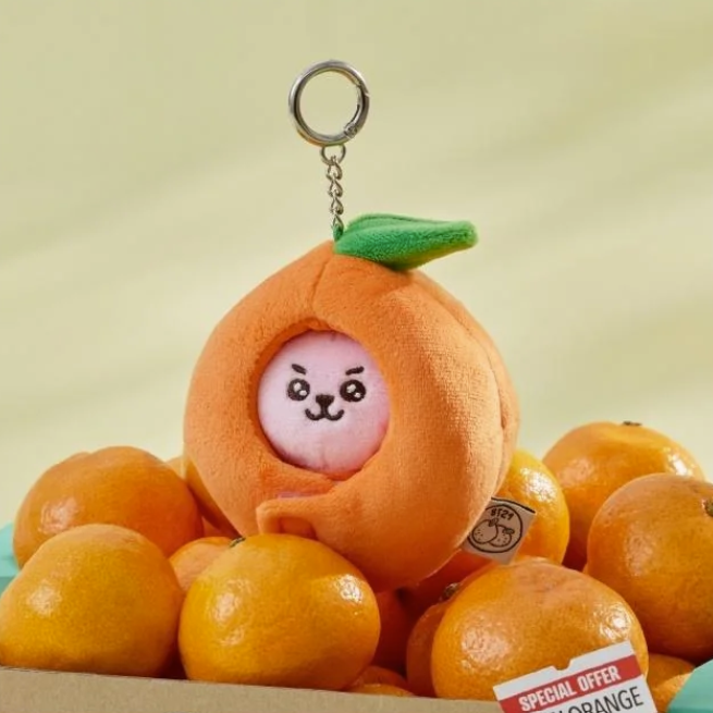 BTS BT21 Cooky Plush keychain shaped like an orange with a face on top of real oranges.
