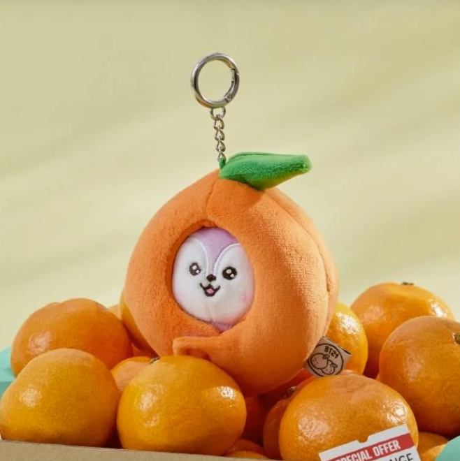 BTS BT21 Mang Plush keychain shaped like a tangerine with a small character inside, surrounded by real tangerines on a light green background.