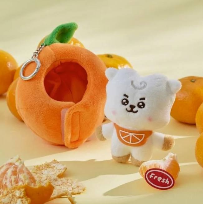 BTS BT21 RJ Plush toy shaped like a mandarin orange with a keychain, surrounded by actual mandarin oranges on a beige background.